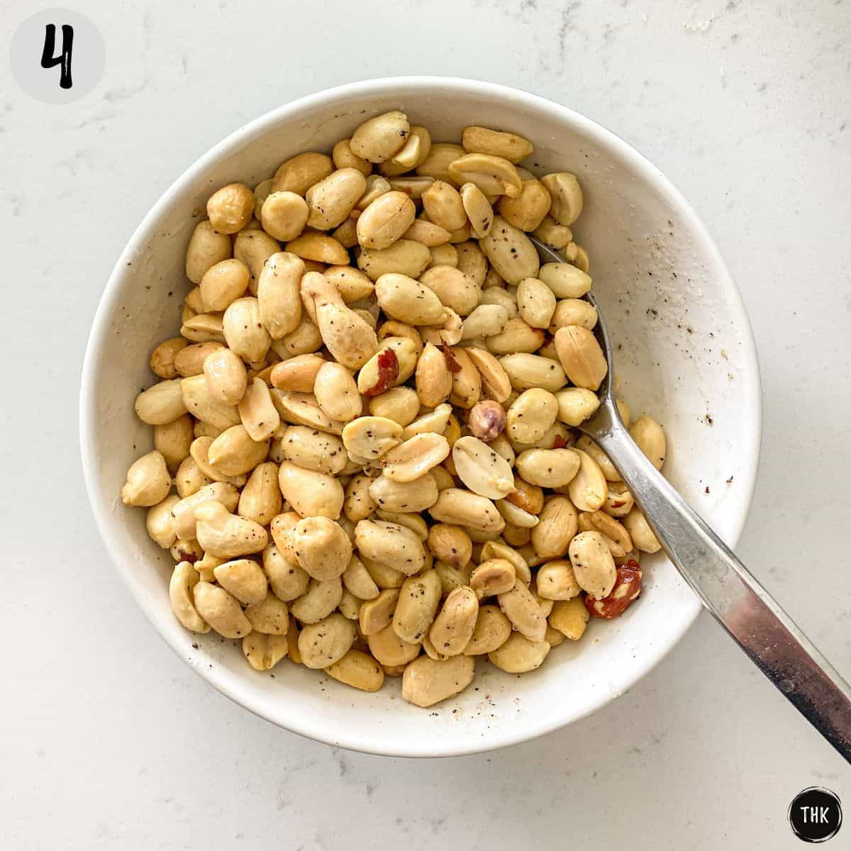 Bowl of peanuts with salt and pepper on top.