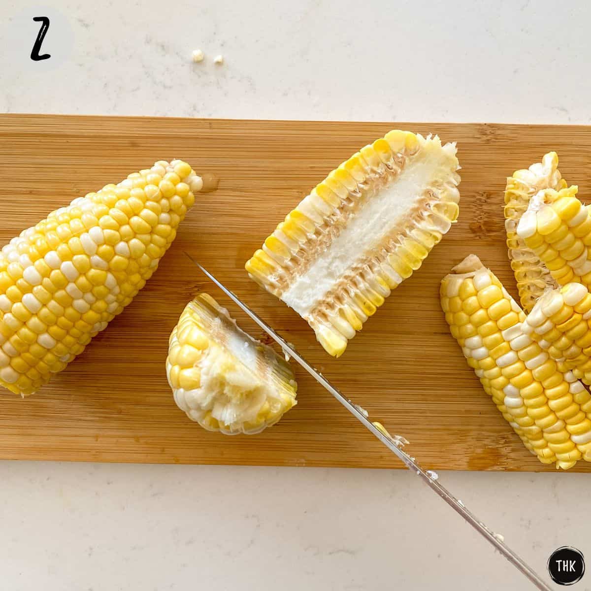 Corn on the cob sliced in half vertically on cutting board.