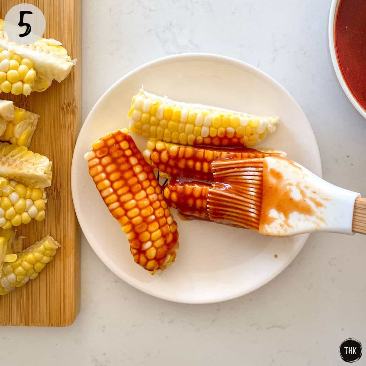BBQ sauce being brushed onto corn on the cob pieces.