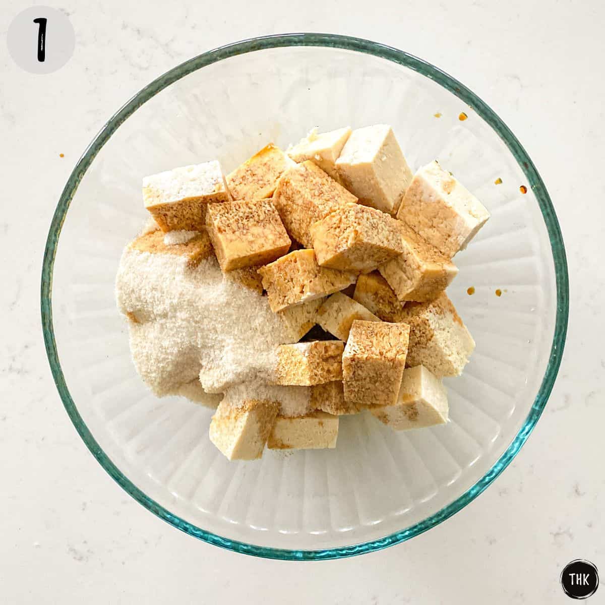 Cubes of tofu in glass bowl with flour on top.