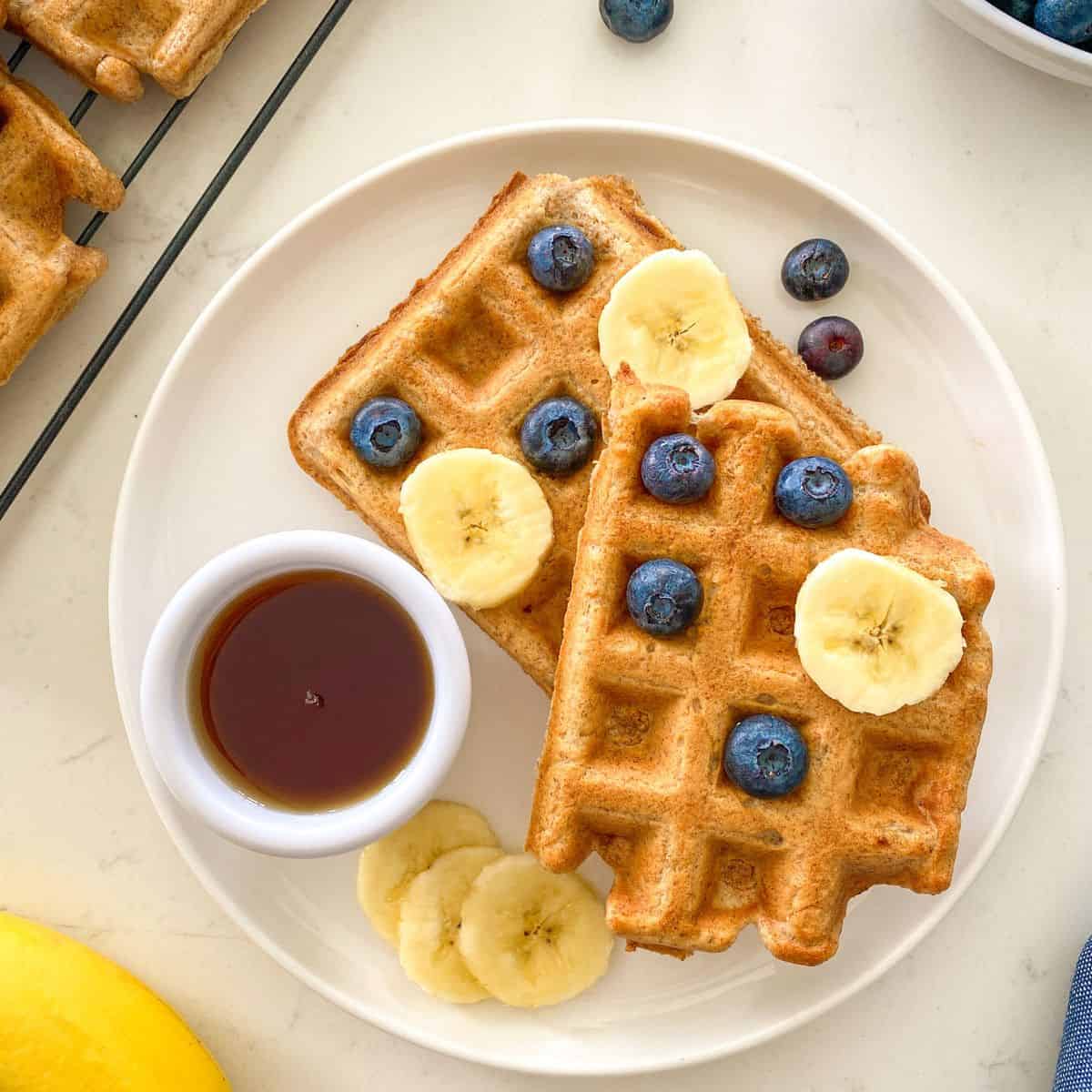 Plate with two waffles, with banana slices and blueberries on top.