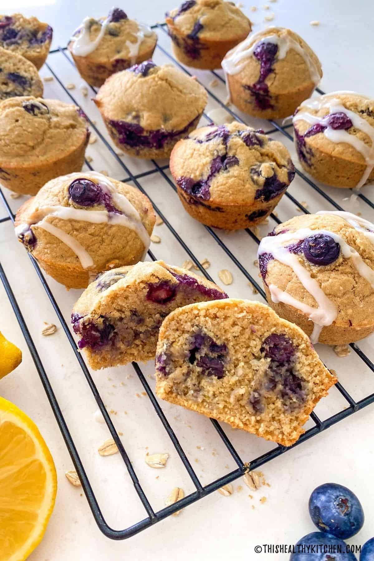 Blueberry muffins on cooling rack with one of them cut in half to expose blueberries inside.