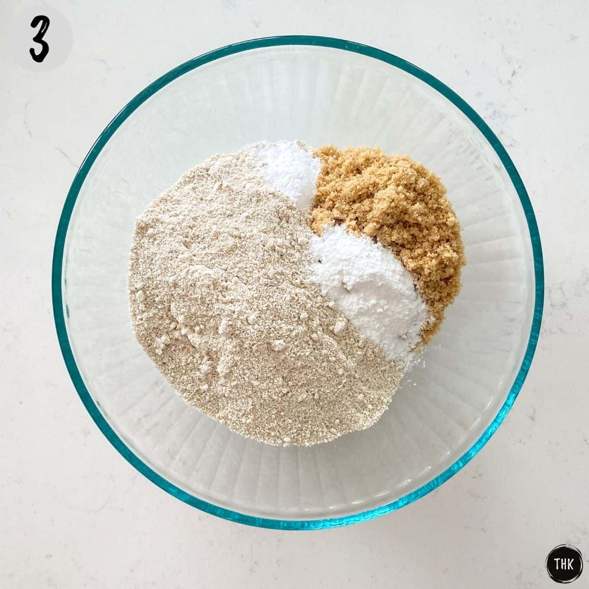 Mixing bowl with oat flour, baking powder, baking soda and brown sugar inside.