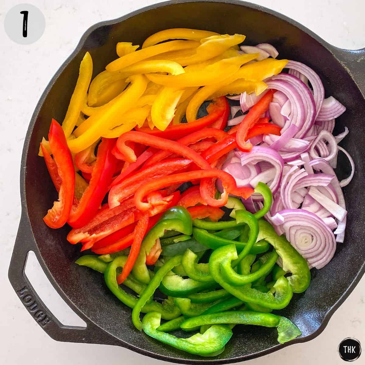 Sliced bell peppers and red onion in cast iron pan.