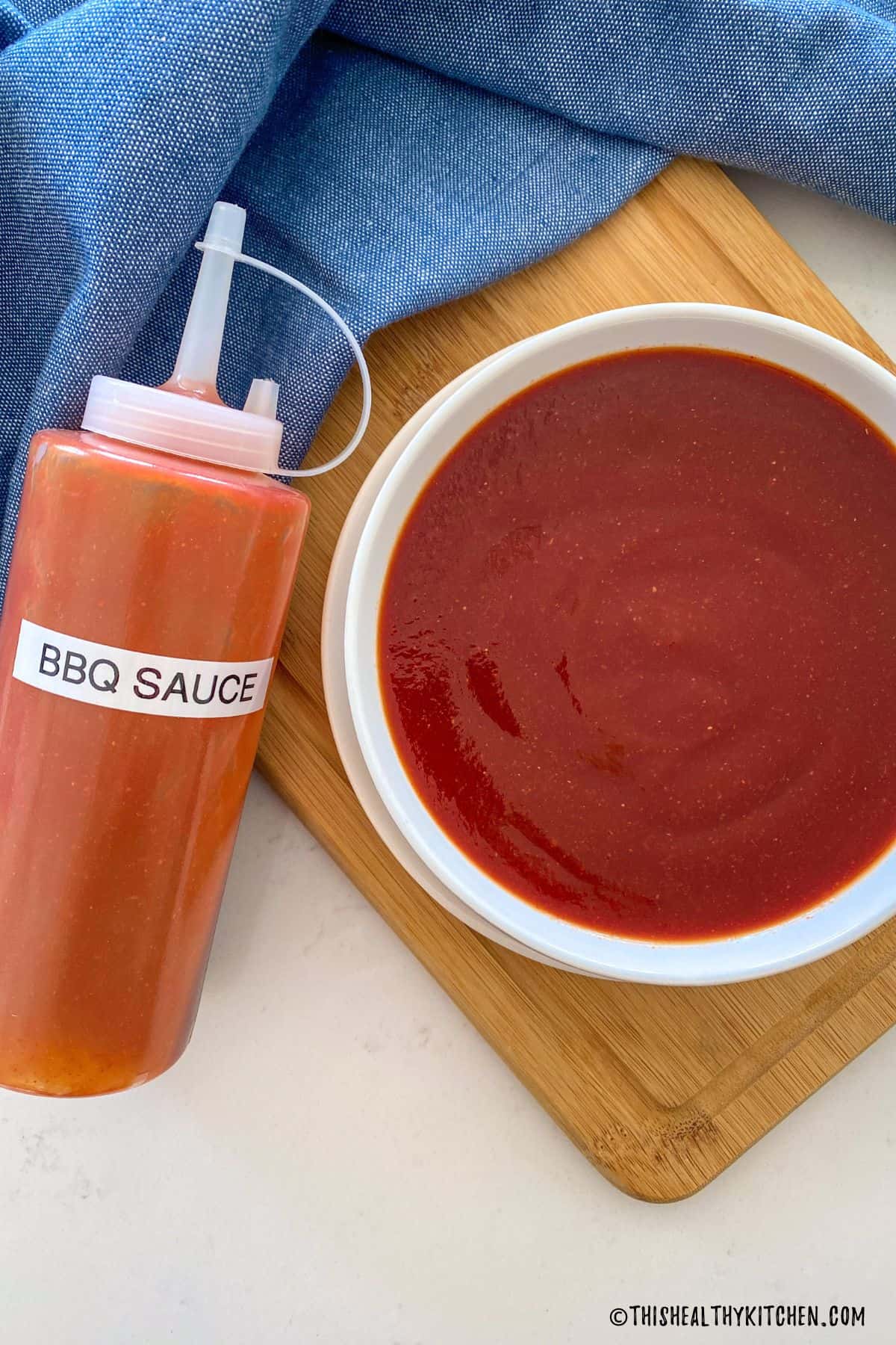 White bowl with red sauce inside and bottle beside it that reads BBQ sauce.