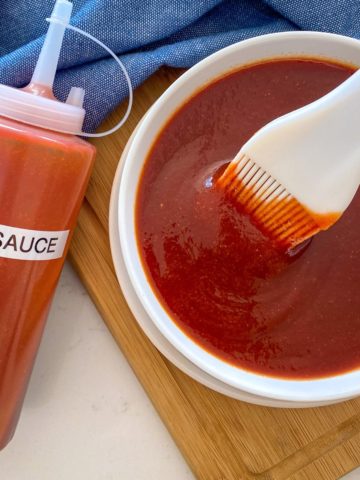 Bowl of BBQ sauce with silicone spatula inside and bottle of more sauce beside it.