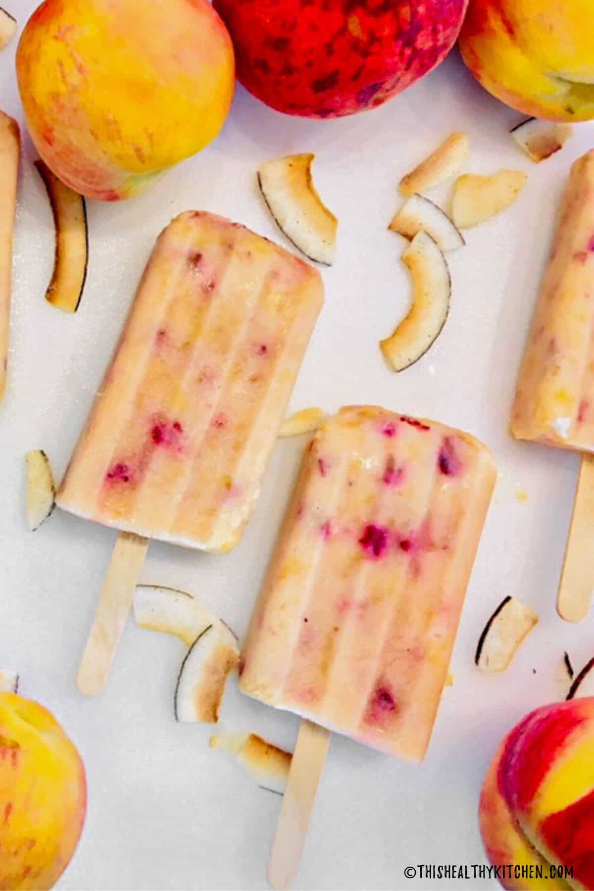 Close up of peach popsicles on white cutting board.