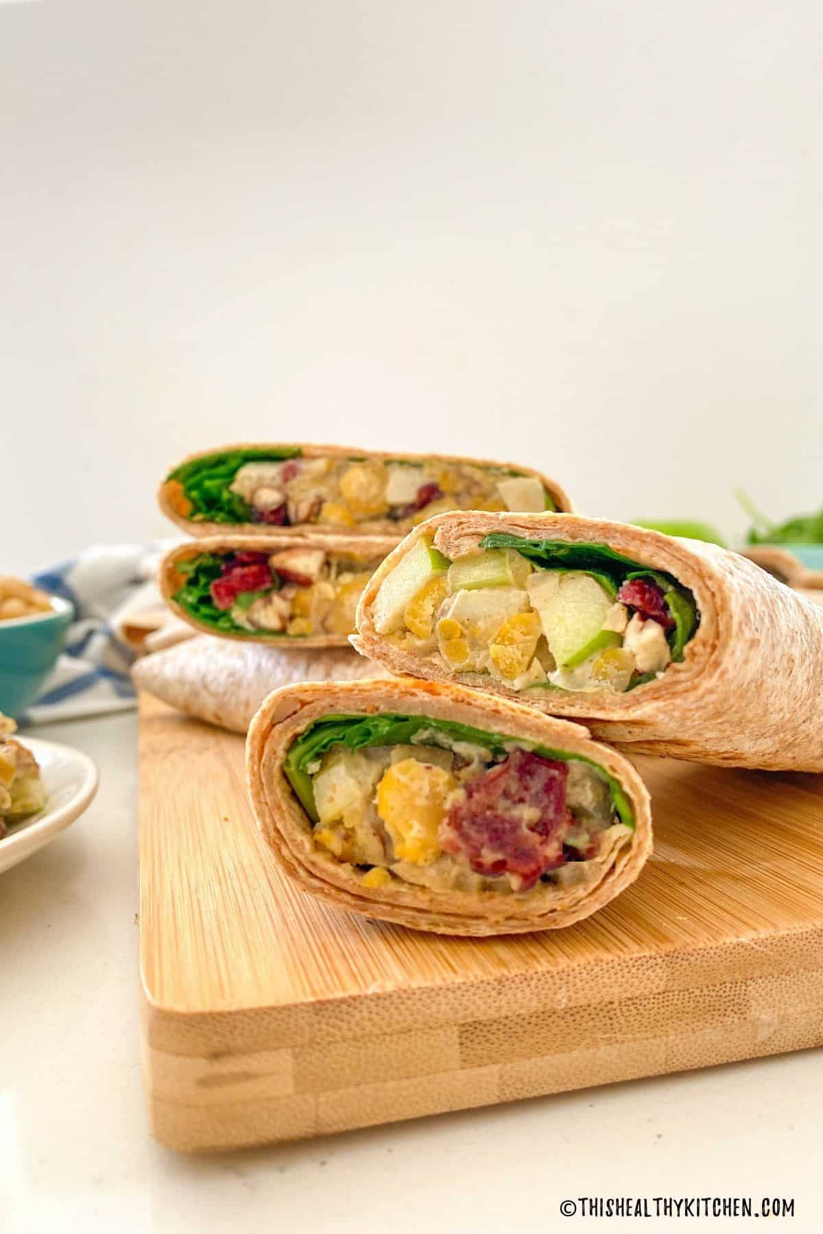 Wraps stuffed with chickpeas, cranberries, apple, celery and spinach sitting on cutting board.