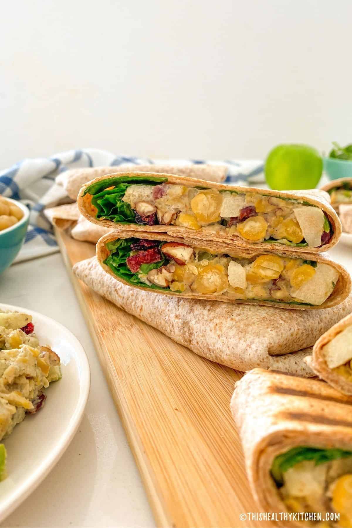 Halved vegan chicken wrap with spinach, chickpeas, apple, pecans and cranberries inside.