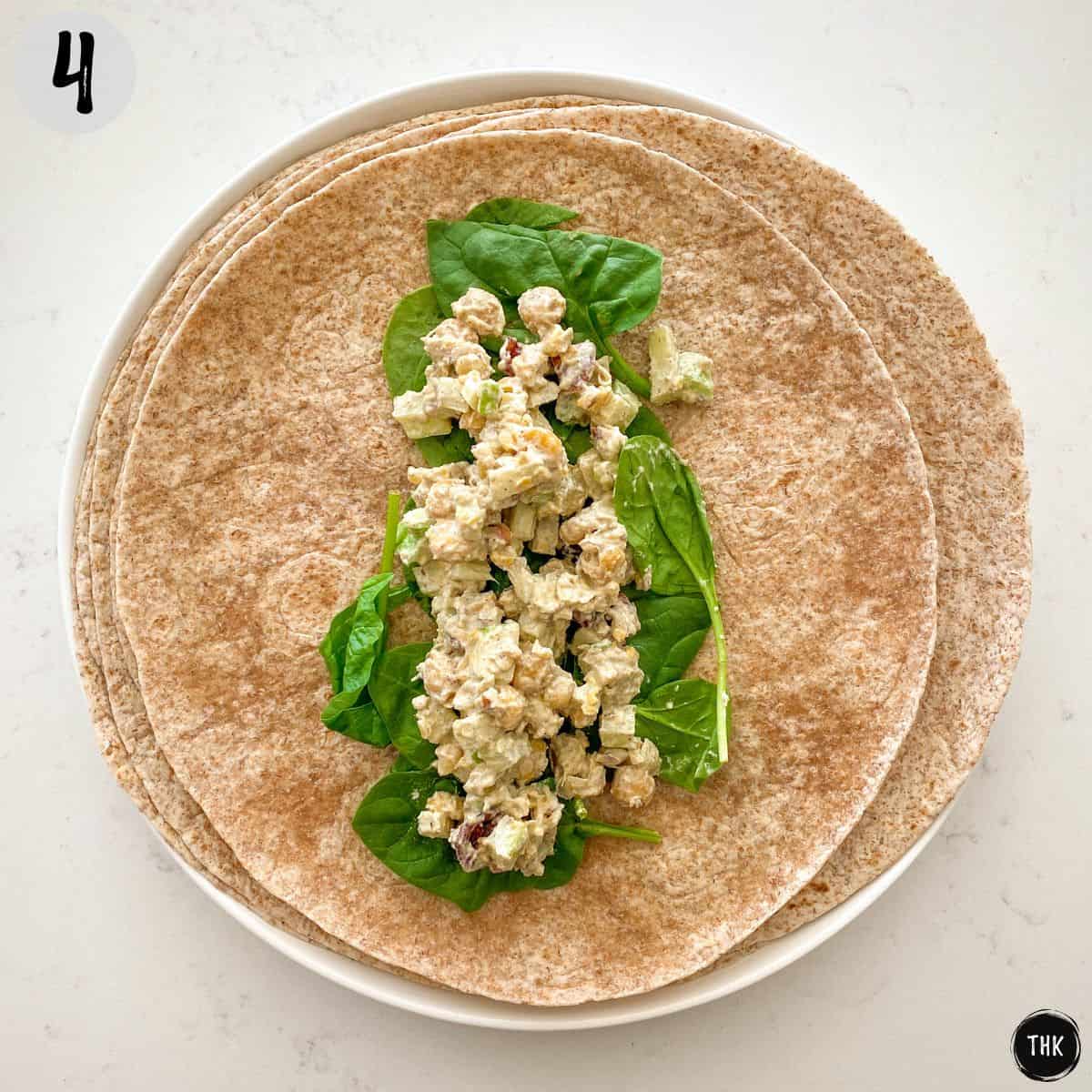 Tortilla wrap open with spinach and chickpea salad in the middle.