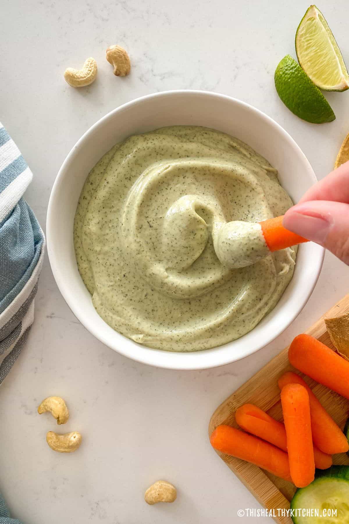 Vegan ranch dip in white bowl with carrot being dipped inside.
