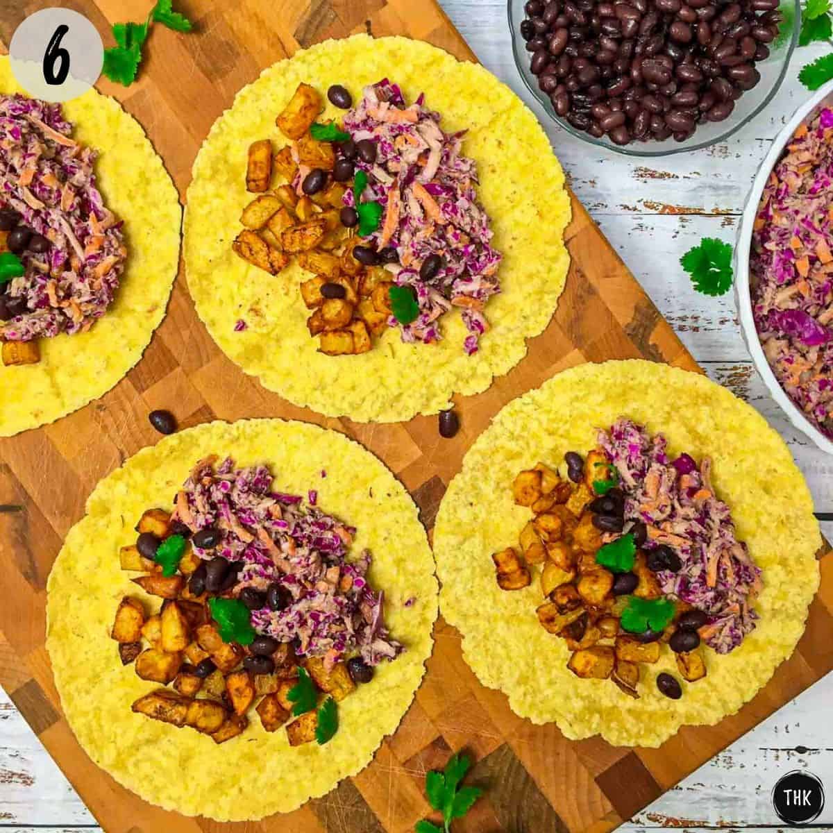 Four open corn tortillas with potatoes, black beans, coleslaw and cilantro on top.