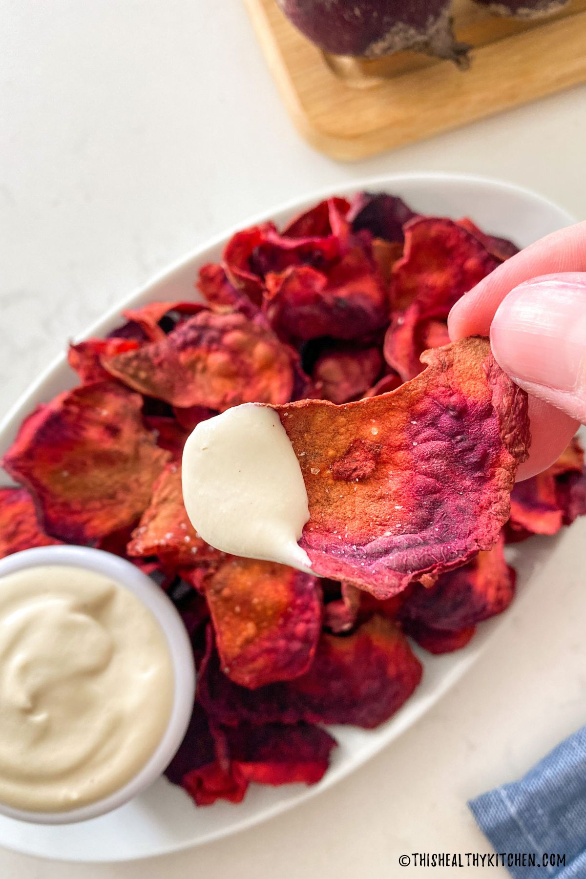 Hand holding up beet chip with white dip on it.