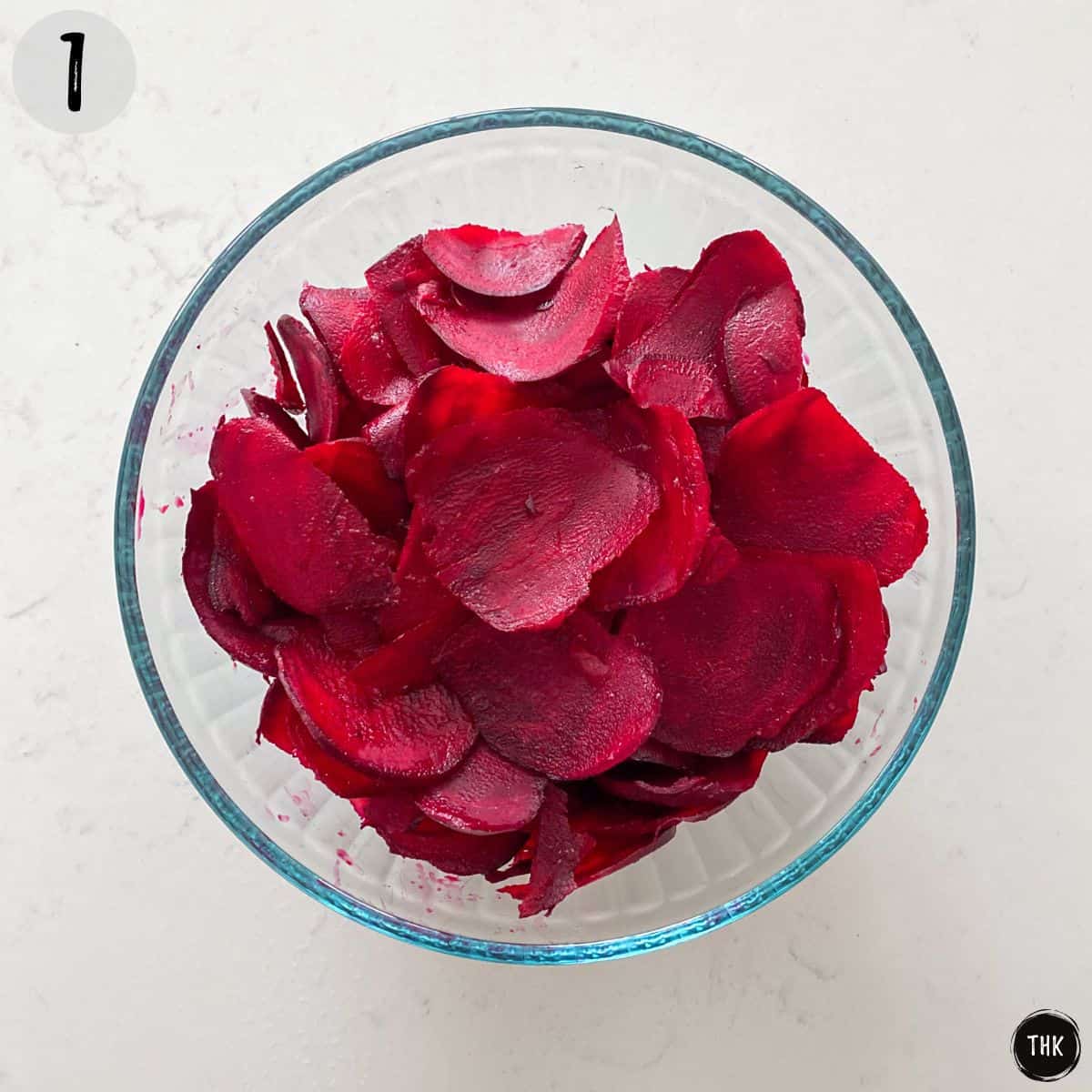 Glass bowl with thinly sliced raw beet chips inside.