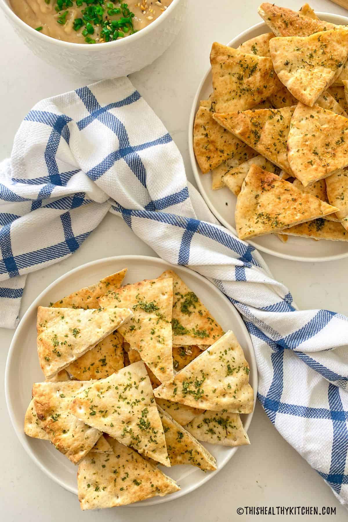 Two plates of air fried pita chips with blue and white dish towel between them.