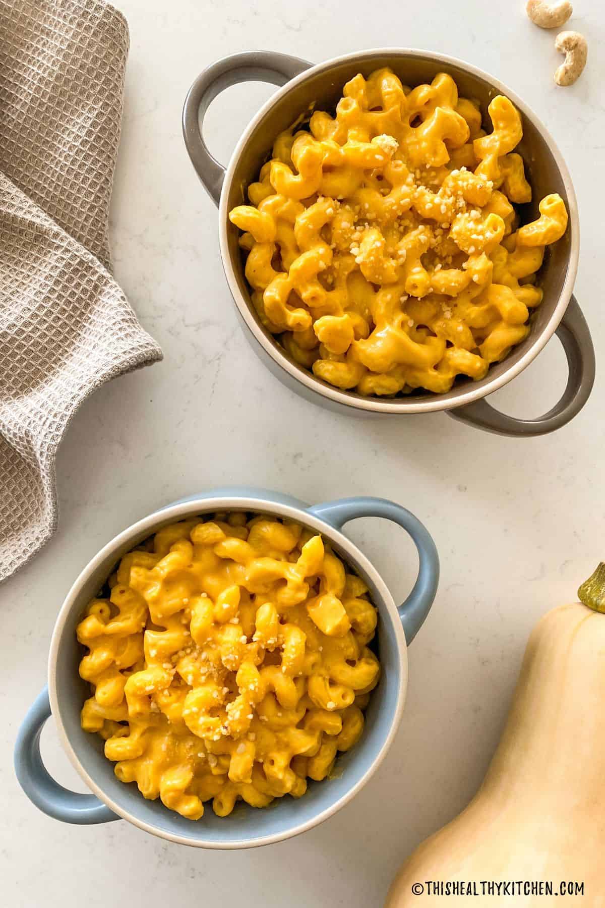Two bowls of mac and cheese with butternut squash beside them.