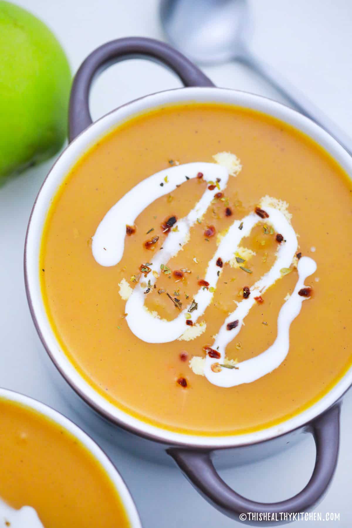 Butternut squash soup with sour cream drizzle and chili flakes on top.