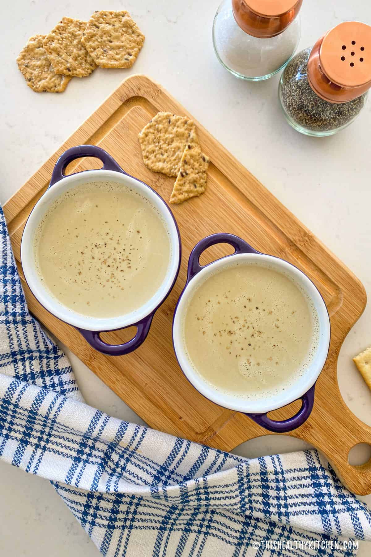 Two bowls of creamy soup with crackers beside them.