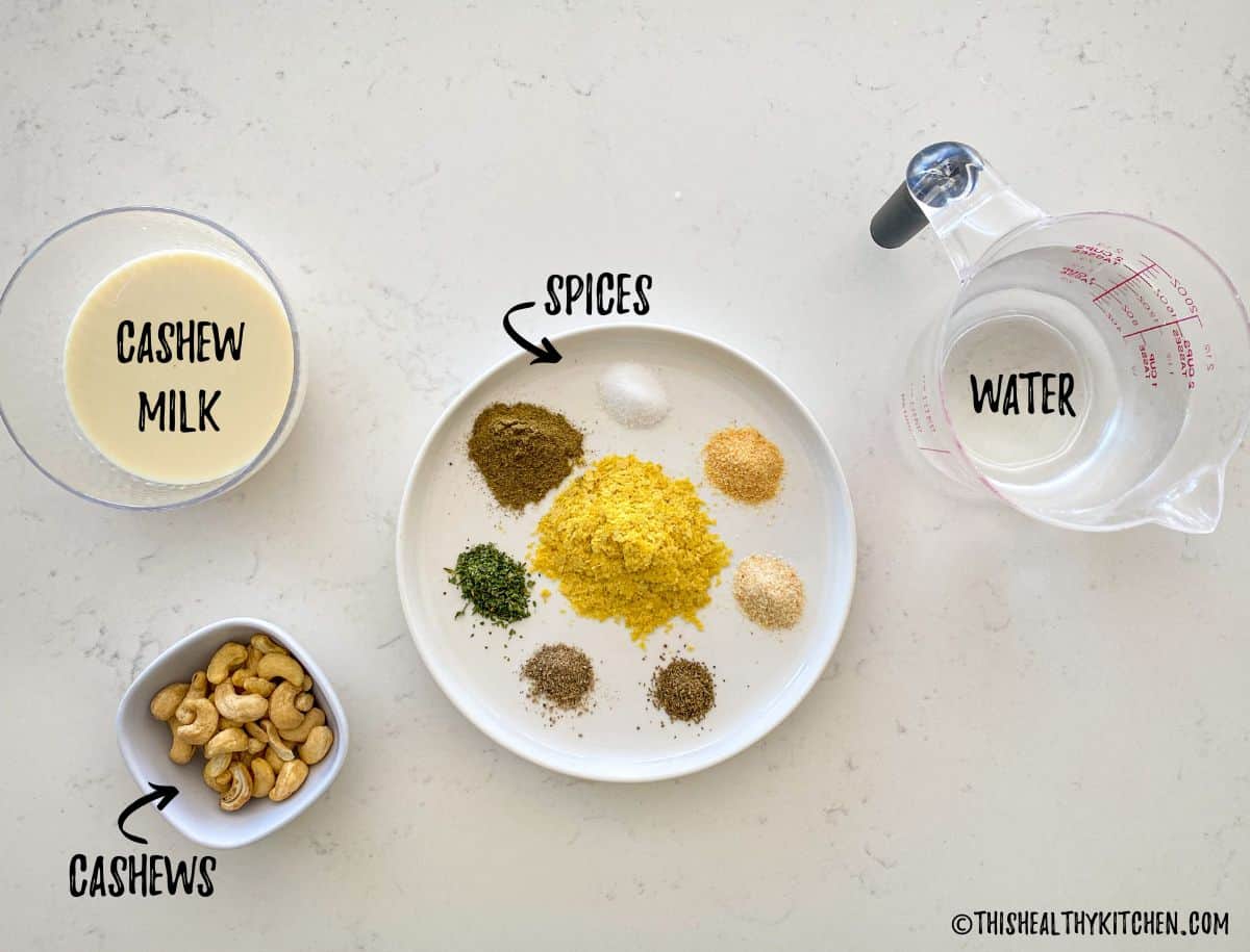 Plate with 8 spices on it, cup of water, cup of milk and bowl of cashews on countertop.