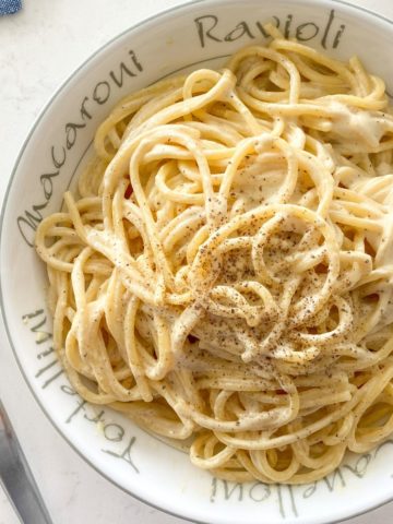 Bowl of spaghetti with white sauce and black pepper on top.