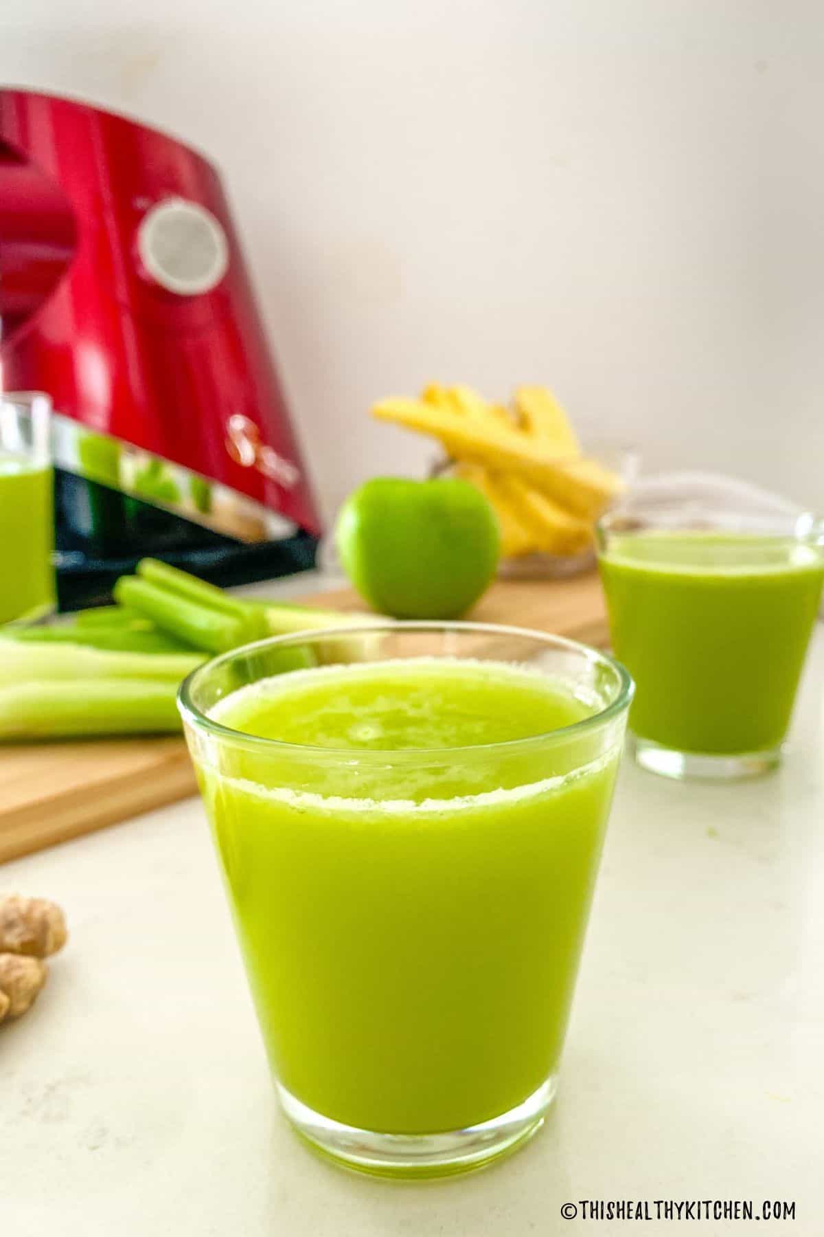 Two cups of green juice with Sana juicer in the background.