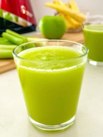 Close up of glass of green juice with Sana juicer in the background.