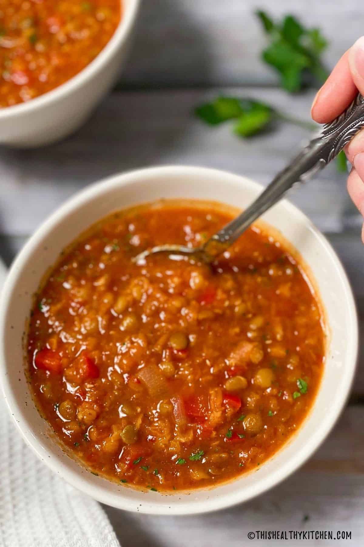 Sloppy joe soup in bowl with hand holding spoon inside.