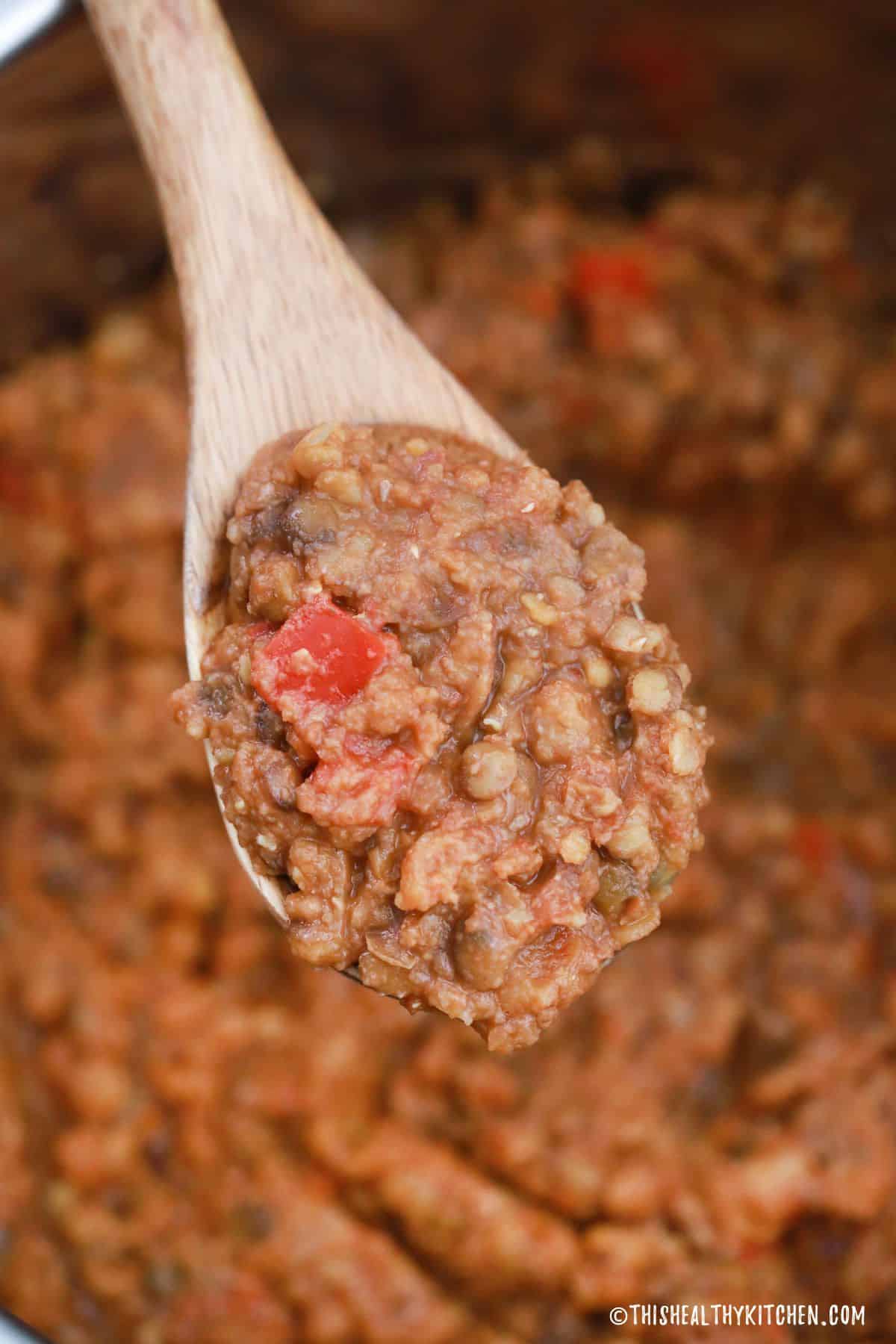 Wooden spoon scooping lentil stew from Instant Pot.