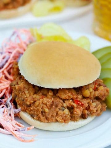 Sloppy joe sandwich with pickles and coleslaw on the side.