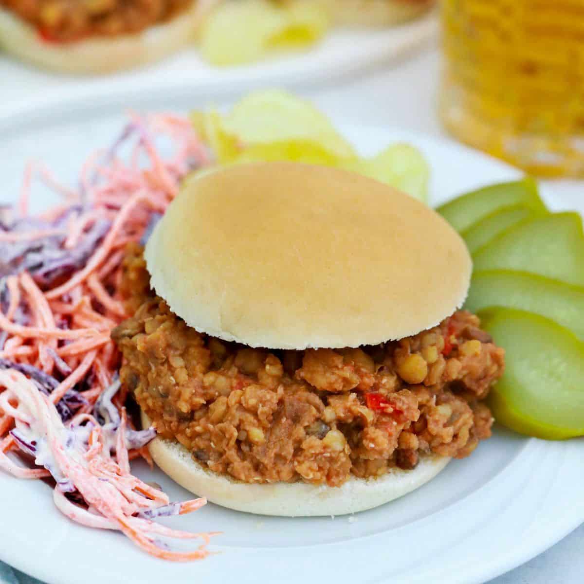 Sloppy joe sandwich with pickles and coleslaw on the side.