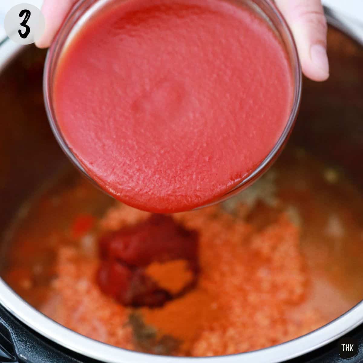 Tomato sauce being poured into pot.