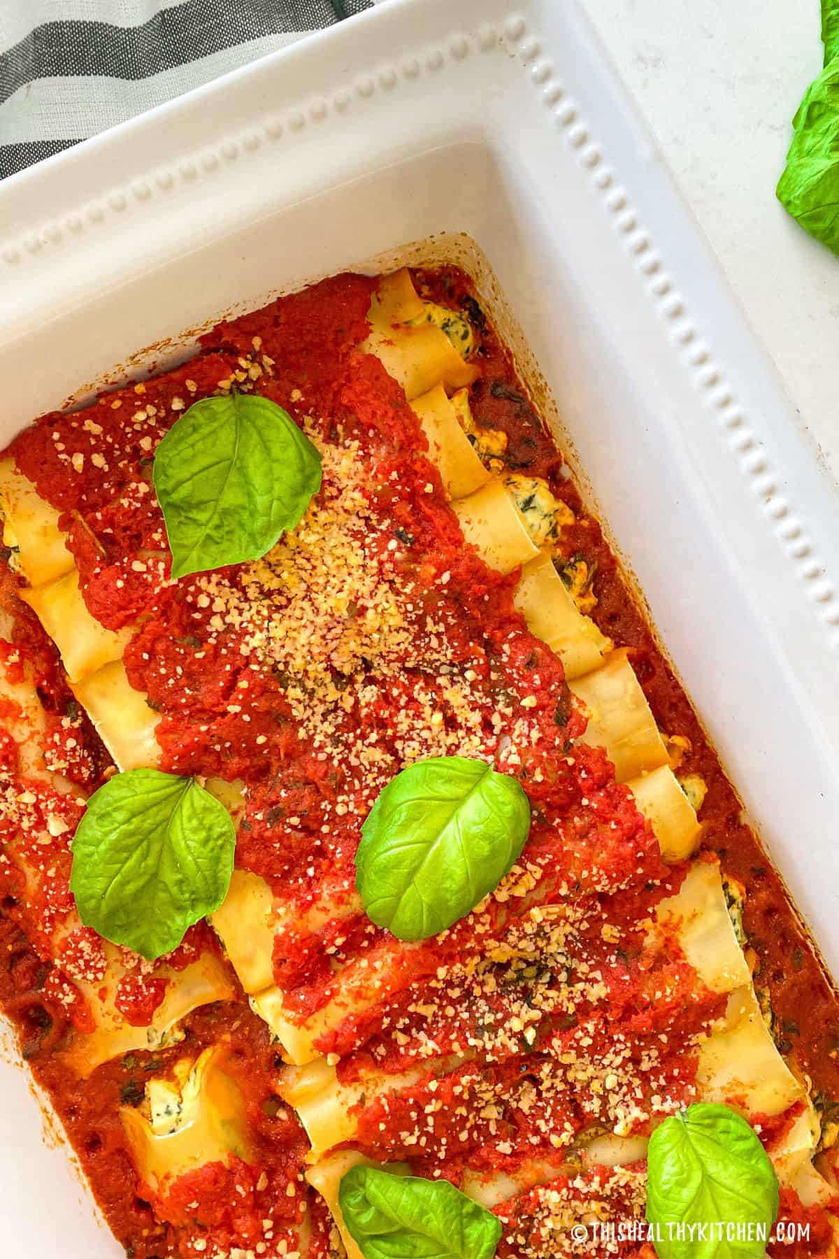 Baking dish with cooked vegan cannelloni inside and basil leaves on top.