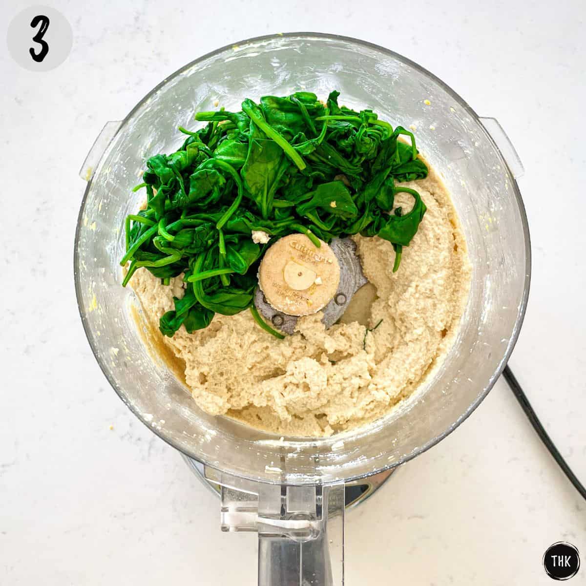 Ricotta cheese mixture in food processor with wilted spinach on top.