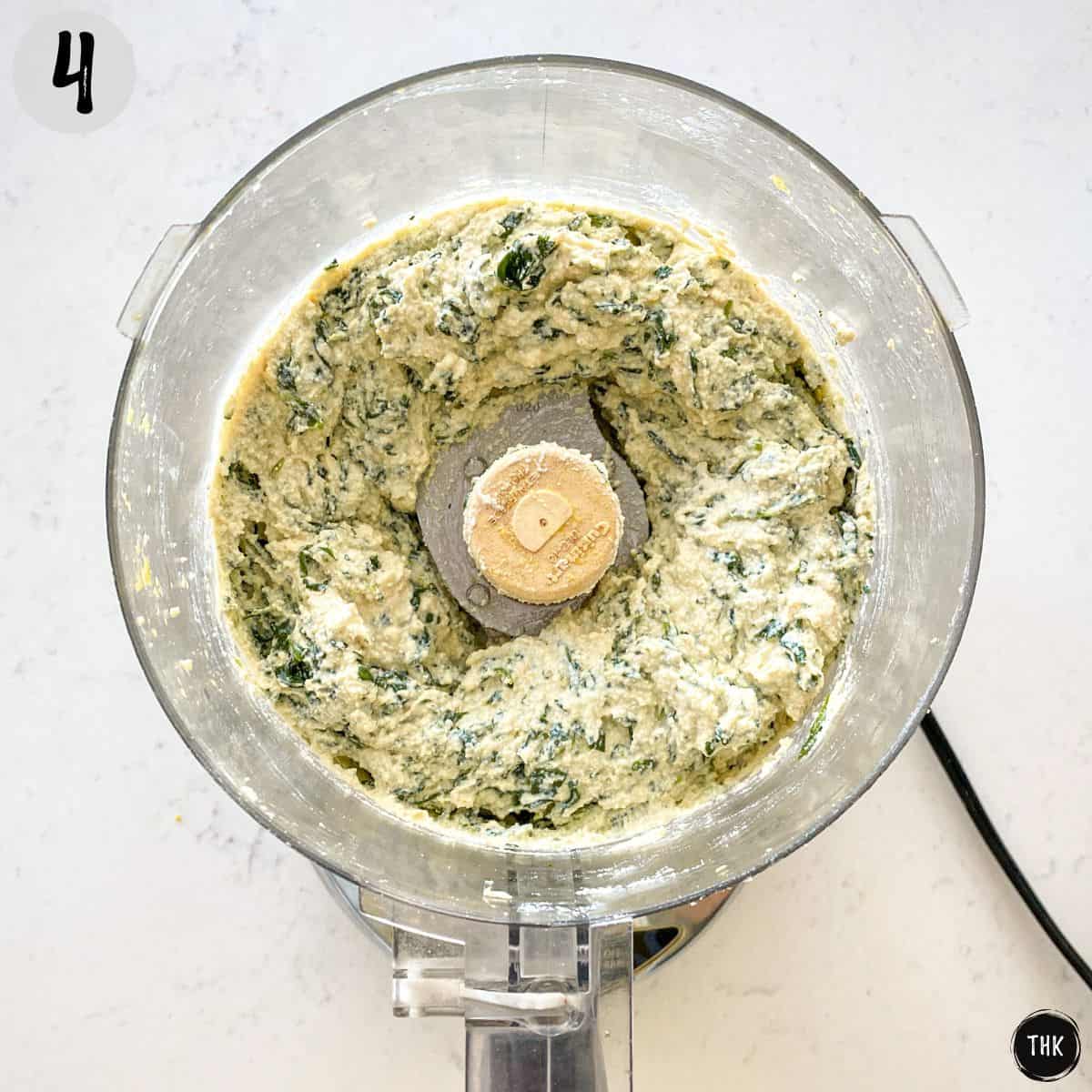 Food processor with vegan ricotta cheese and spinach inside.