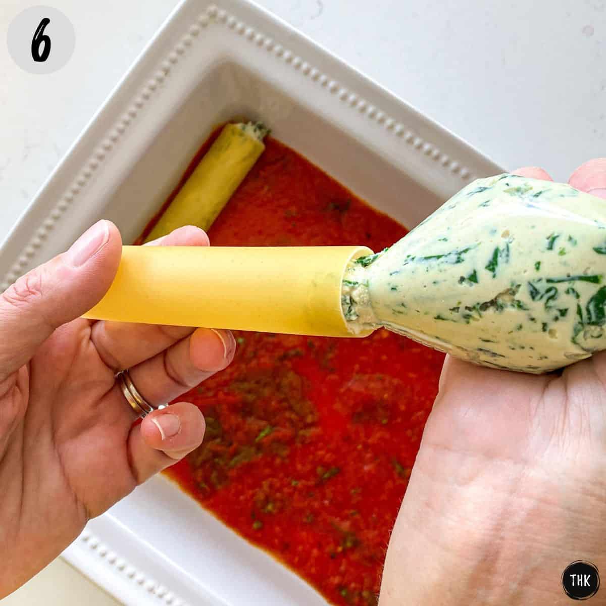 Hand stuffing cannelloni shell with cheese filling from piping bag.
