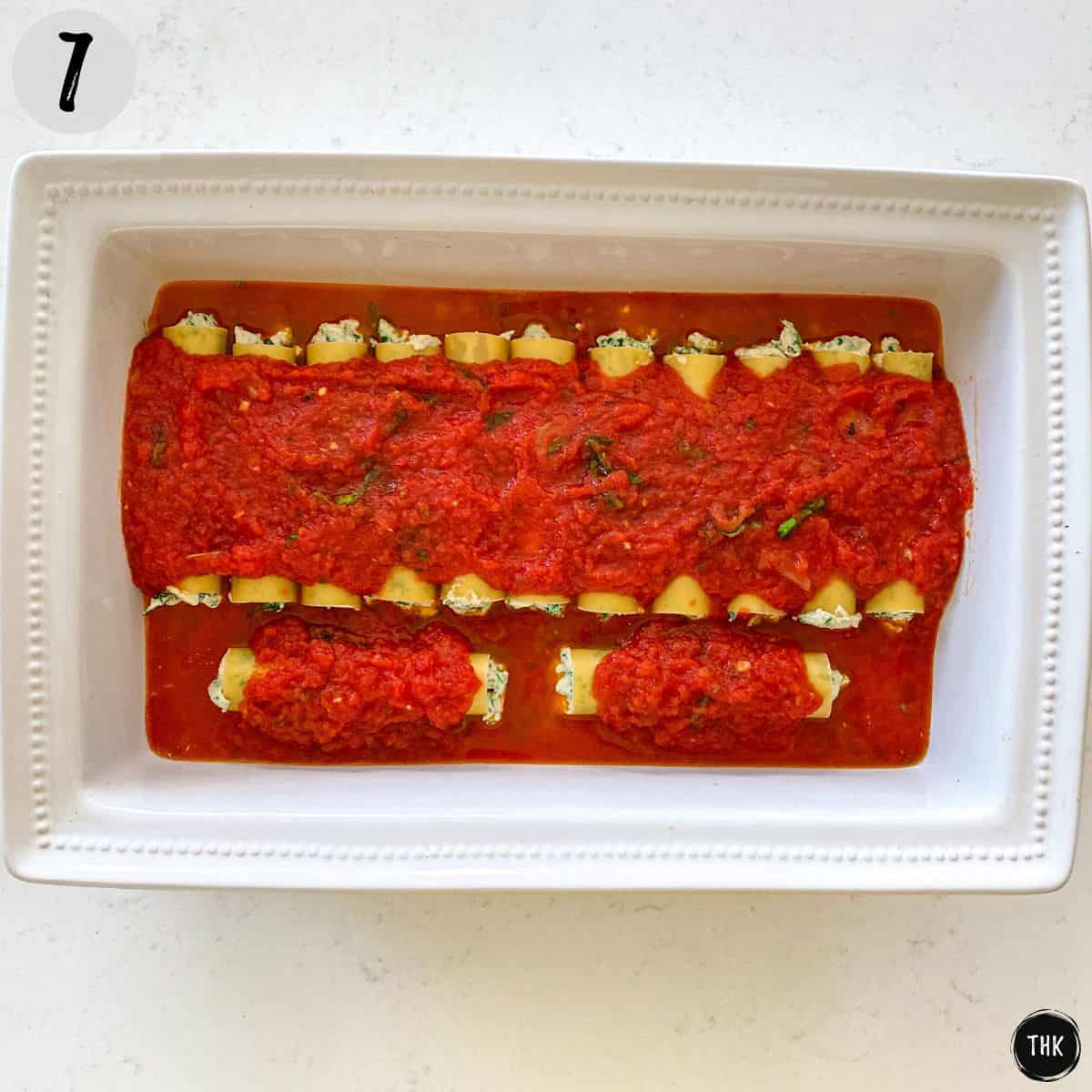 Cannelloni in baking dish covered in tomato sauce.