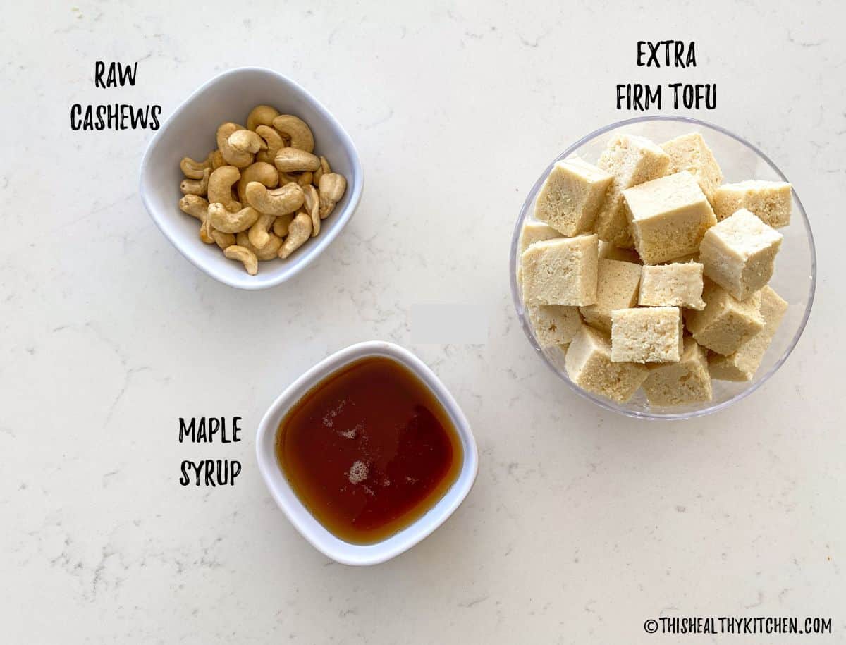 Bowls of tofu cubes, raw cashews and maple syrup on kitchen counter.