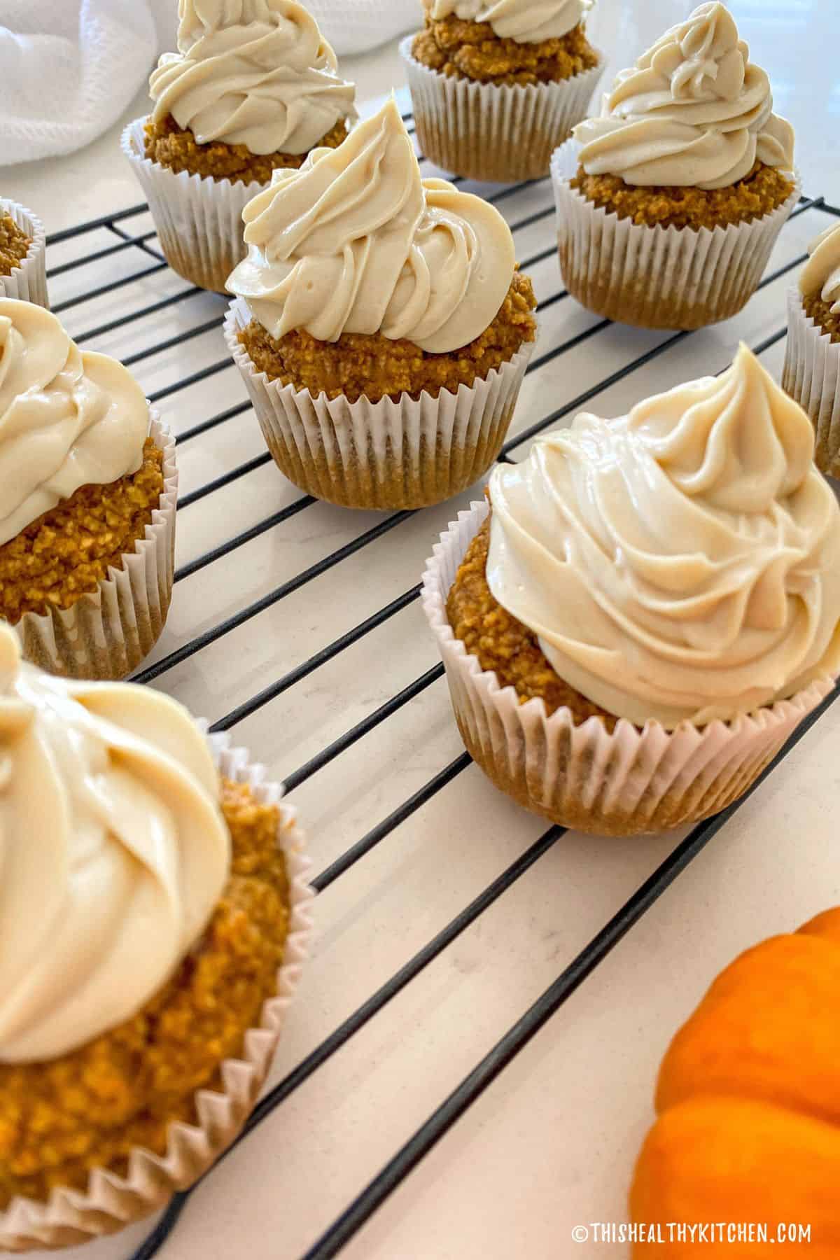 Frosted cupcakes on cooling rack with decorative pumpkin on the side.