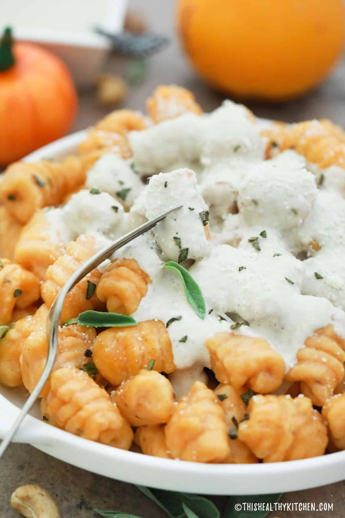 Pumpkin gnocchi in white plate with white sauce and sage on top.