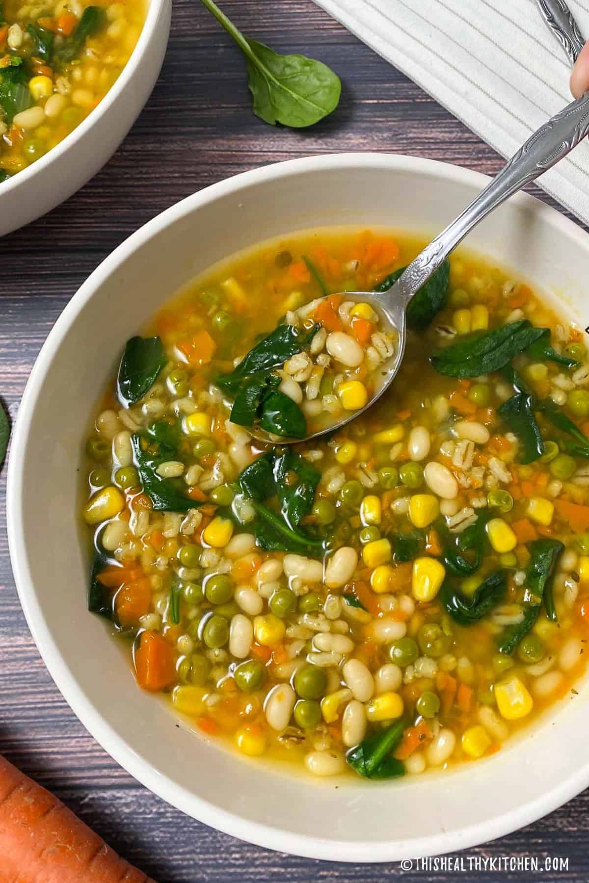Bowl of soup with barley, beans, vegetables and spinach.
