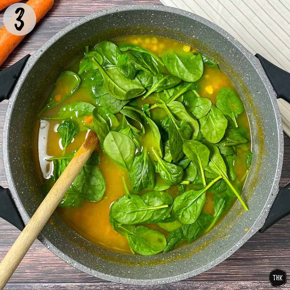 Pot of soup with fresh baby spinach leaves added.
