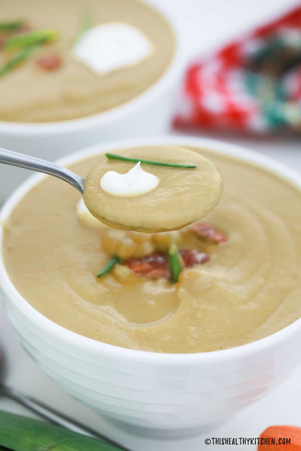 Spoonful of creamy soup being held above bowl of soup.