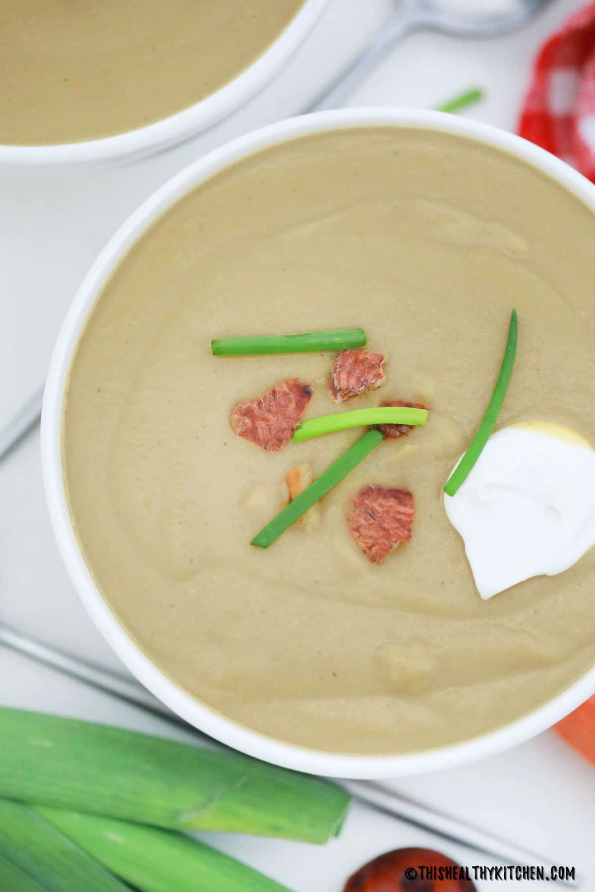 Bowl of creamy brown soup with green onion and chestnut pieces on top.