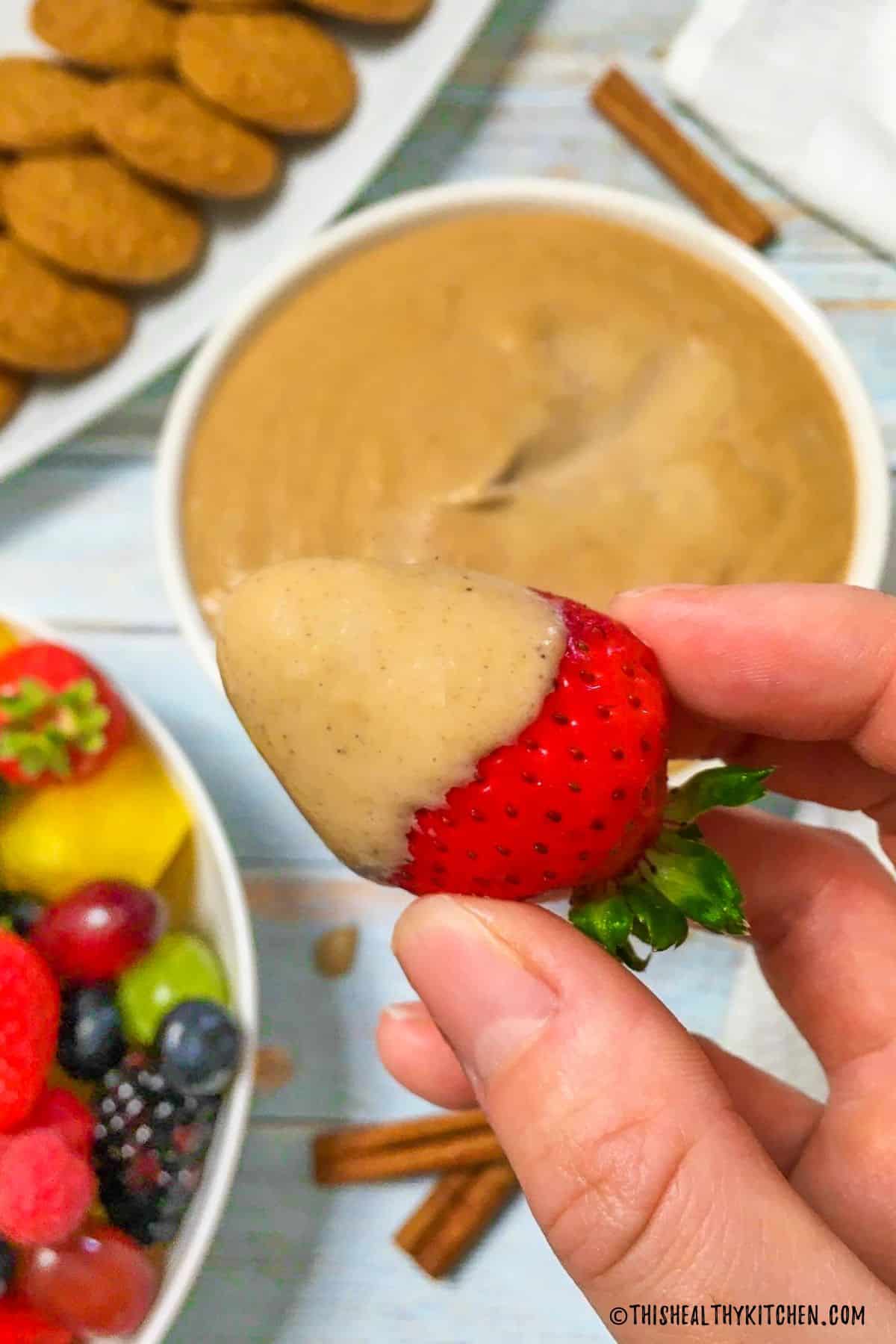 Strawberry being held over bowl of sweet dip that has been dunked inside it.