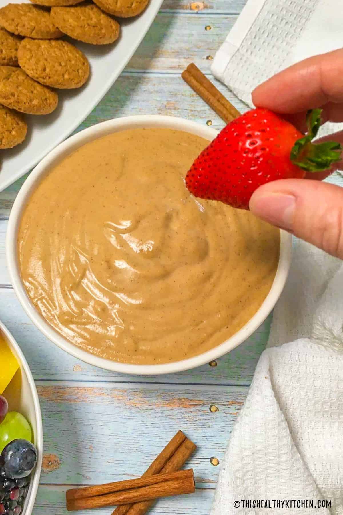 Hand holding strawberry over bowl of dip.