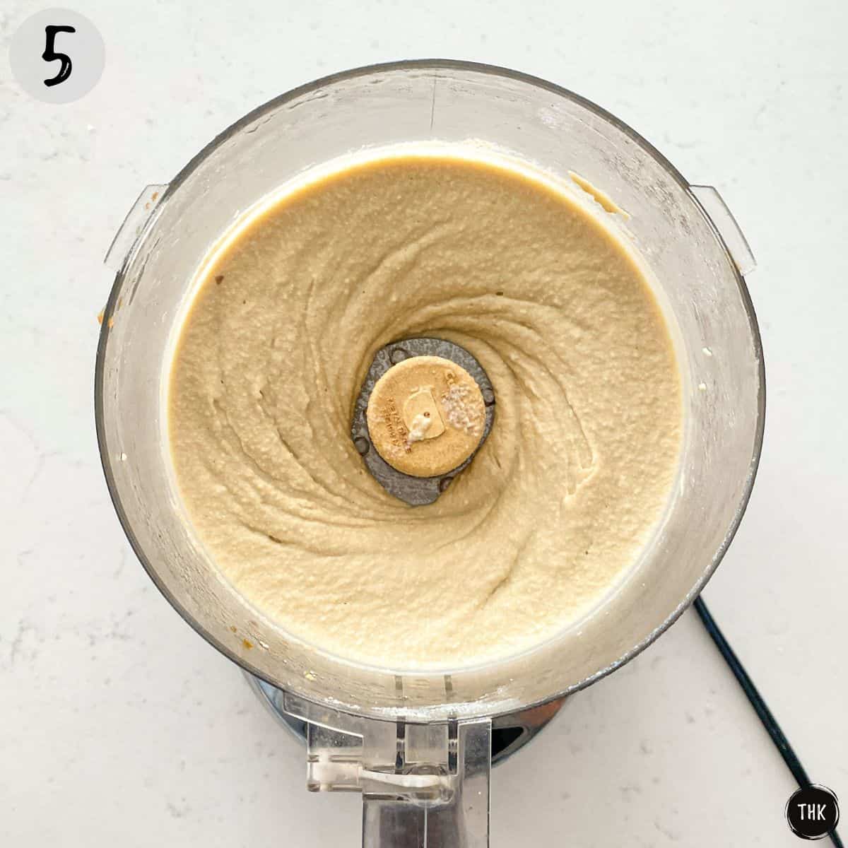 Creamy white pureed mixture inside bowl of food processor.