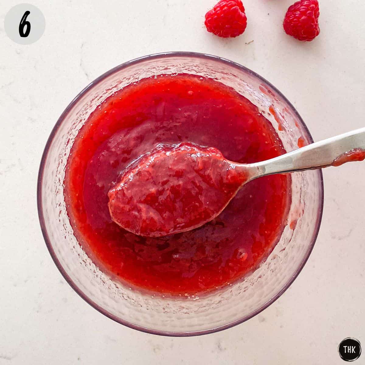Raspberry puree inside small glass bowl with spoon on top.