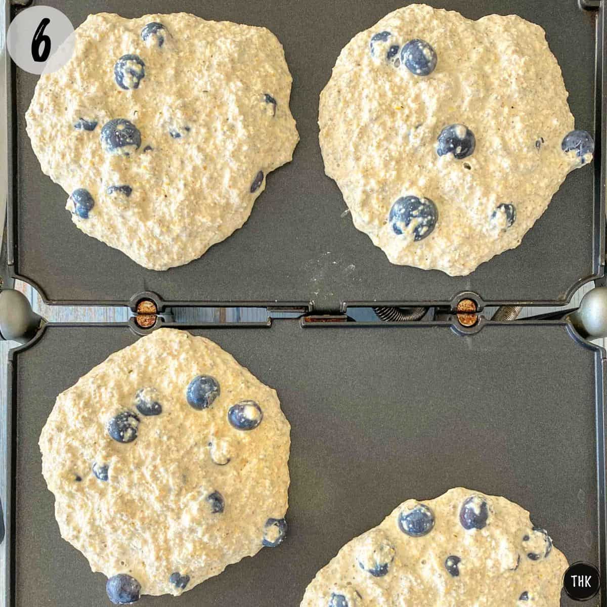 Blueberry pancakes being cooked on griddle.