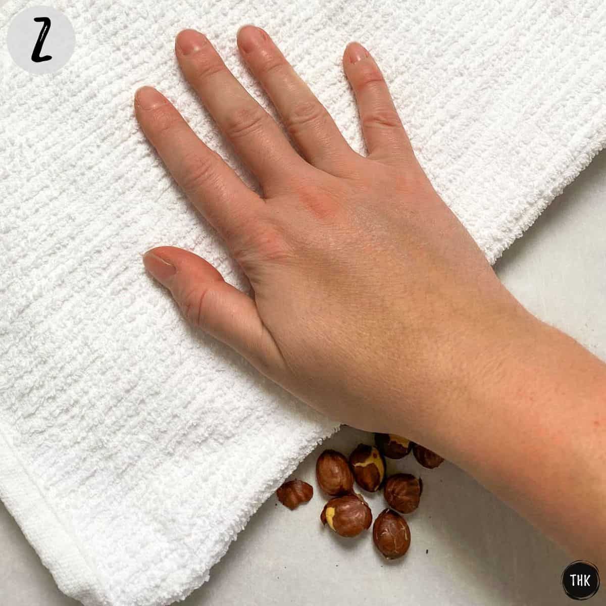 Dish towel being rubbed over tray of roasted hazelnuts.