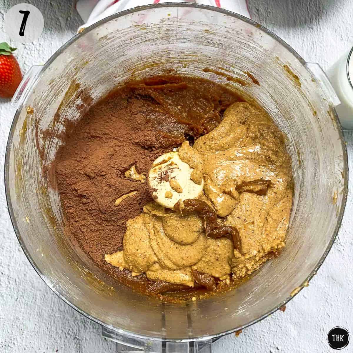 Date paste, hazelnut spread, and cocoa powder in bowl of food processor.